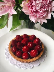 Raspberry chocolate tart on a white plate, in front of pink flowers