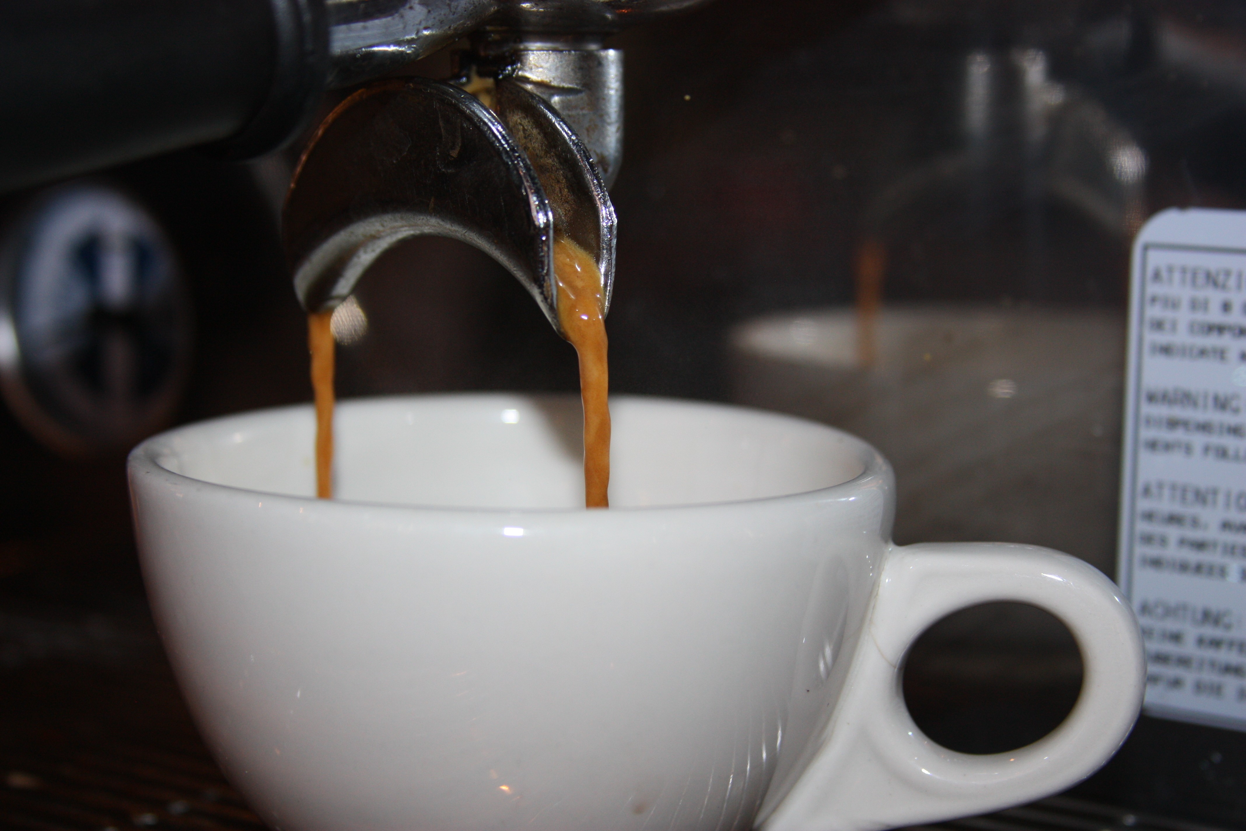 Double shot of espresso pours from a portafilter into an ivory cup.