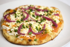Flatbread topped with smoked salmon, hard boiled egg, pickled red onion, and chives.