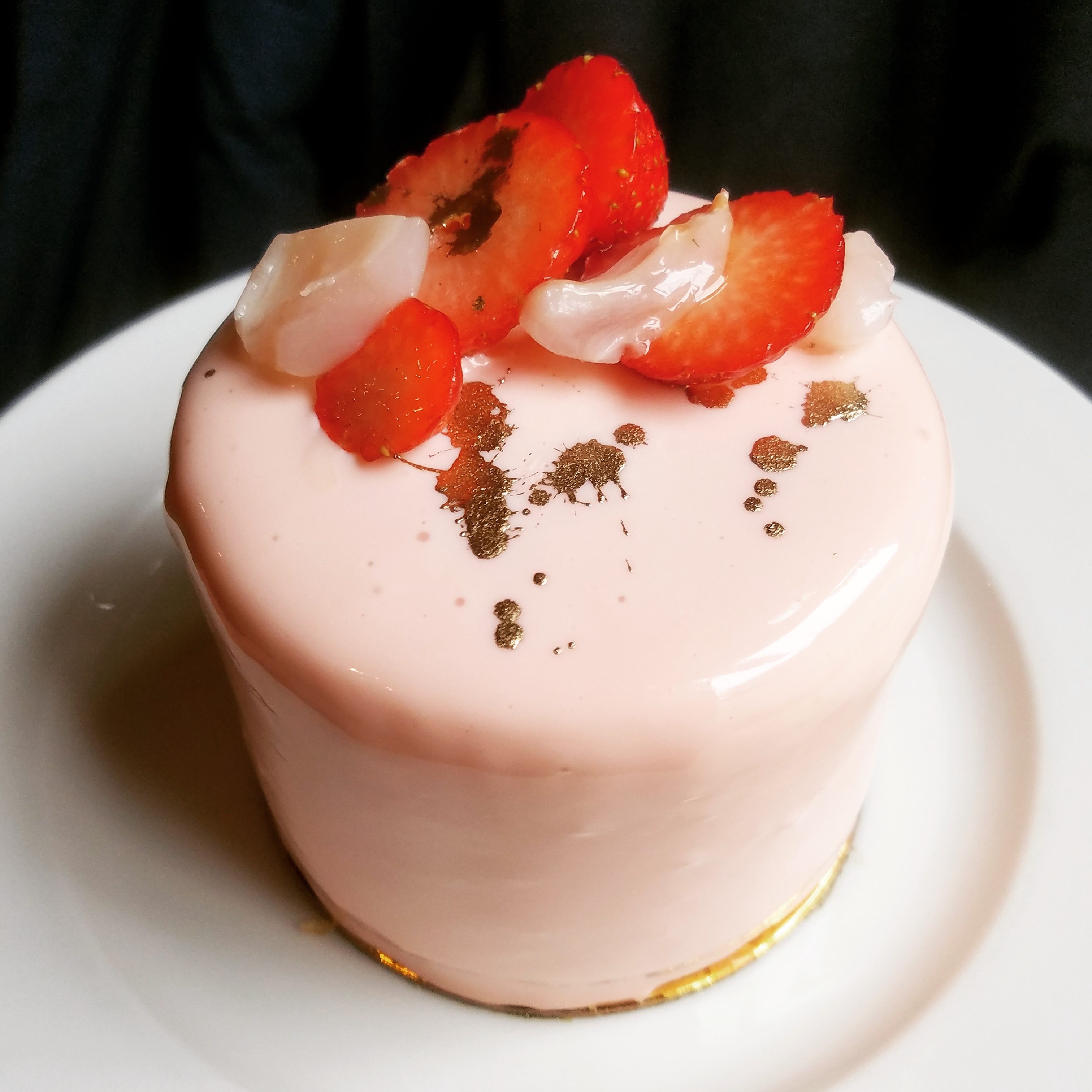 Strawberry rose lychee entremet, covered with pink glaze, on a white plate.