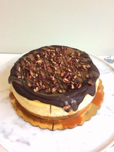 Vanilla cheesecake topped with chocolate, caramel, and pecans