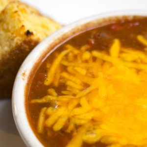Bowl of chili topped with melted cheddar, and two slices of cornbread