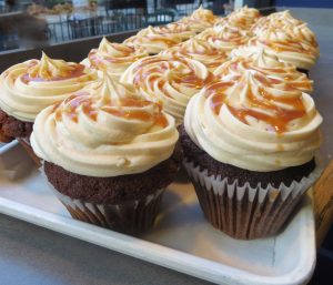 Tray of pumpkin spice apple cupcakes frosted with cream cheese and drizzled with caramel