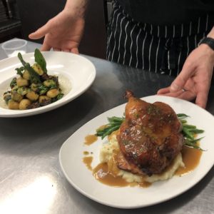 kitchen team presents plates of gnocchi and roasted chicken